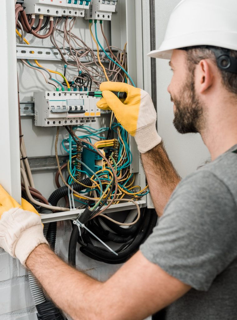 side view of electrician repairing electrical box and using screwdriver in corridor